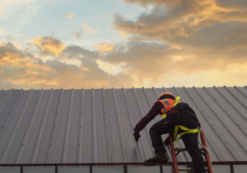 Expert Commercial Roof Repair Services by Story Roofing Roofer in high-visibility gear using a tool to repair a metal roof on a commercial building during a sunset.