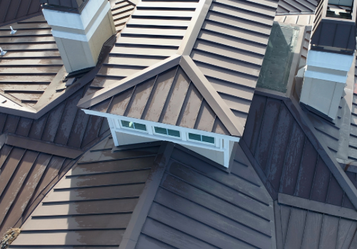 Standing Seam Steel Roofing by Story Roofing Aerial view of a complex roof with standing seam steel panels, featuring multiple chimneys and geometric shapes.