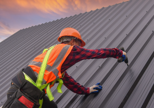 Expert Commercial Roof Installation Services by Story Roofing Professional roofer installing a metal roof on a commercial building at sunset, wearing safety gear.